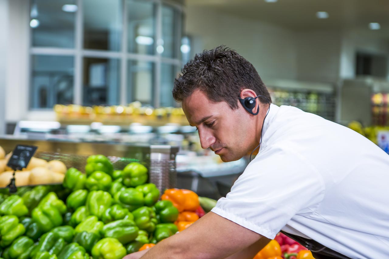 supermarkt medewerker bij de groenteafdeling met het oortje van een portofoon in het oor van retail